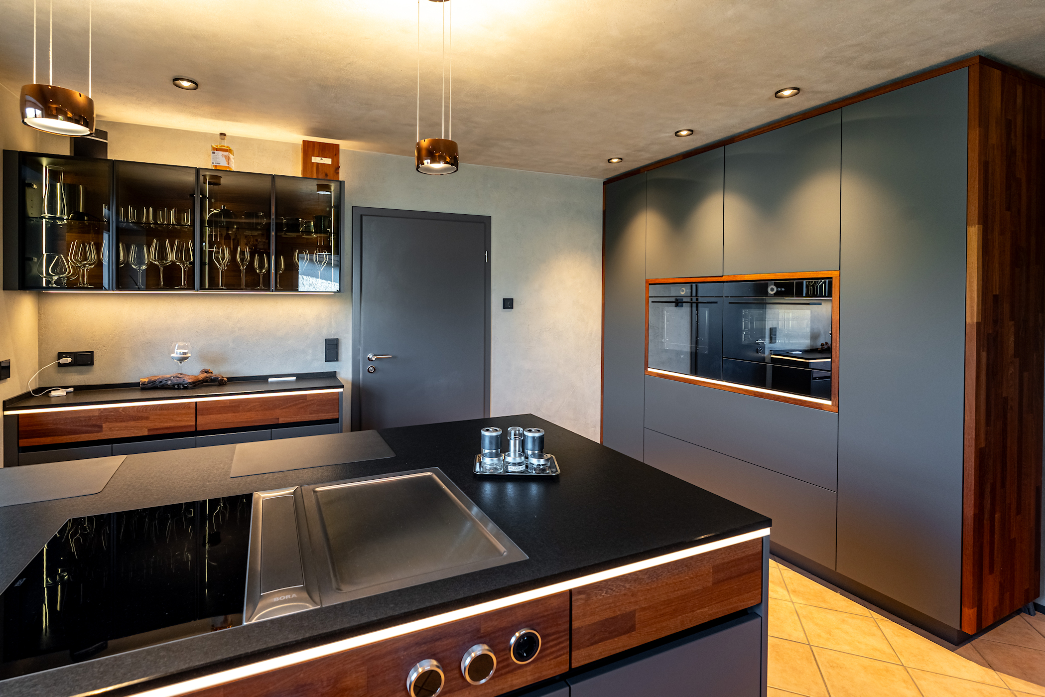 Küche mit Kochfeld im Vordergrund und Wandschrank in Anthrazit und Braun