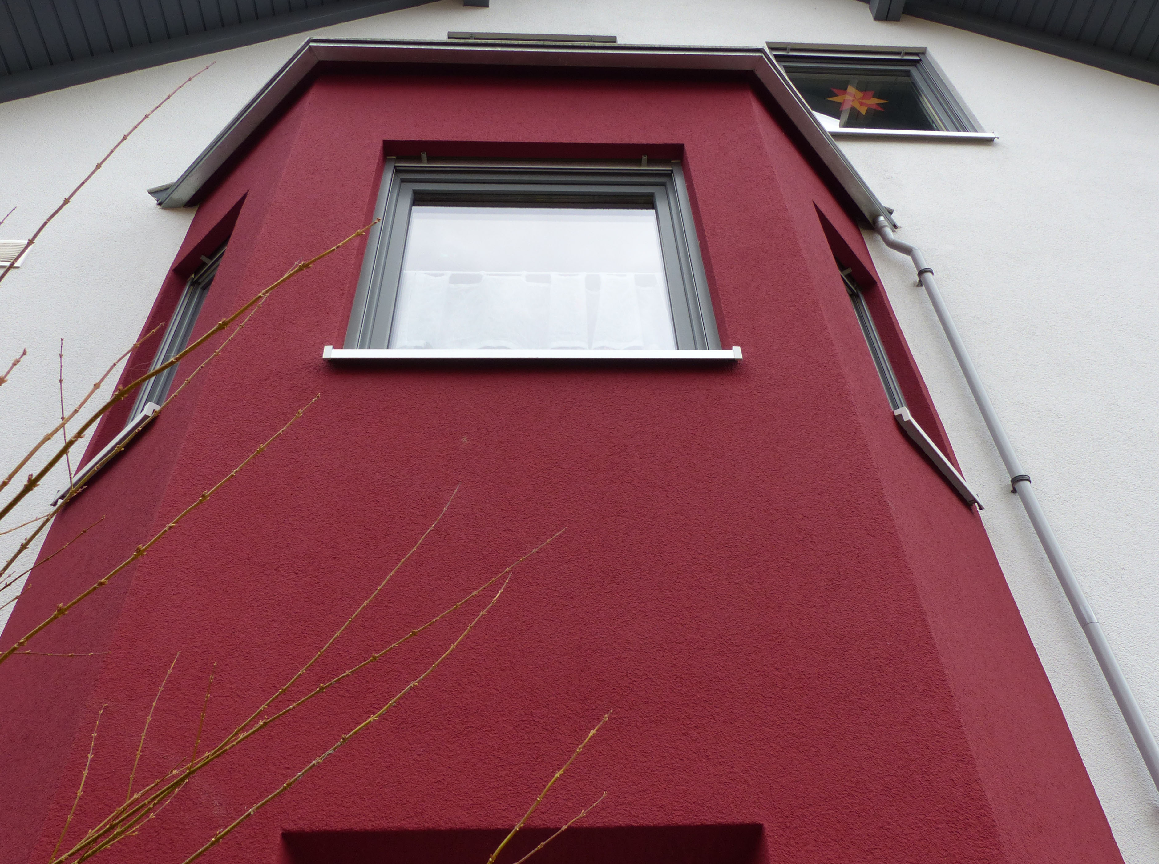 Detailansicht von weinrotem Erker an einer weißen Hausfassade.